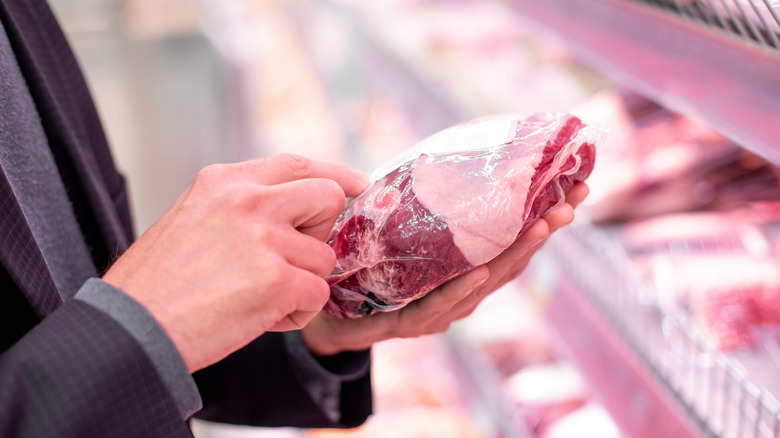 A hand testing a steak's tenderness to gauge freshness