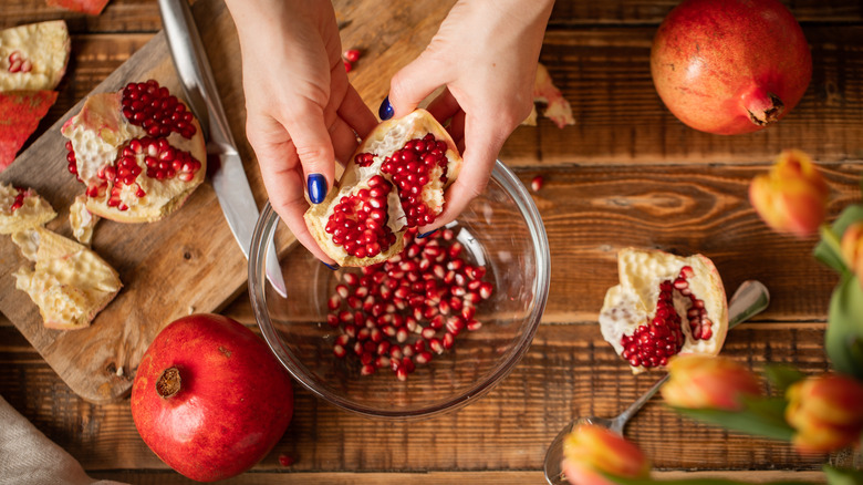 person holding and peeling pomegranate over a bowl