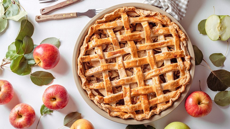 Baked apple pie with lattice crust surrounded by whole apples