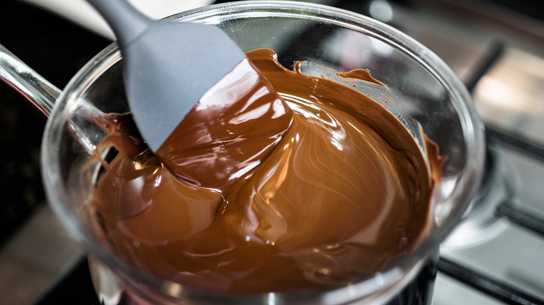 Photo of tempered chocolate in a glass bowl on top of a stovetop saucepan