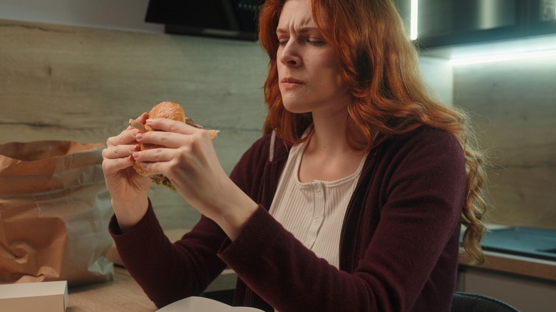 Diner eating a burger with a frown