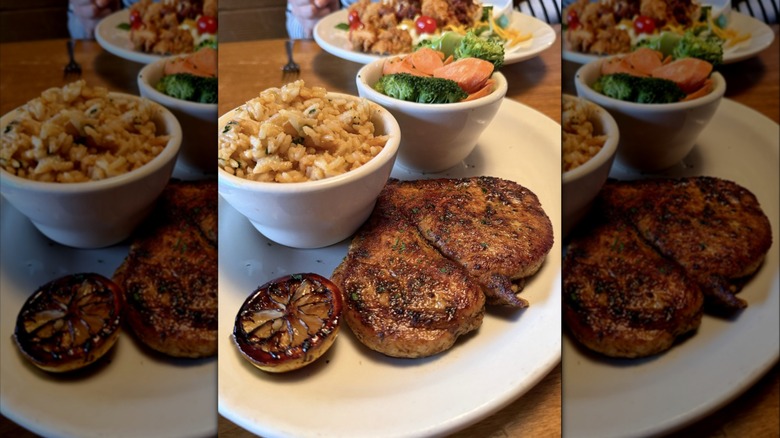 Texas Roadhouse herb crusted chicken in a plate with two bowls of rice and vegetables