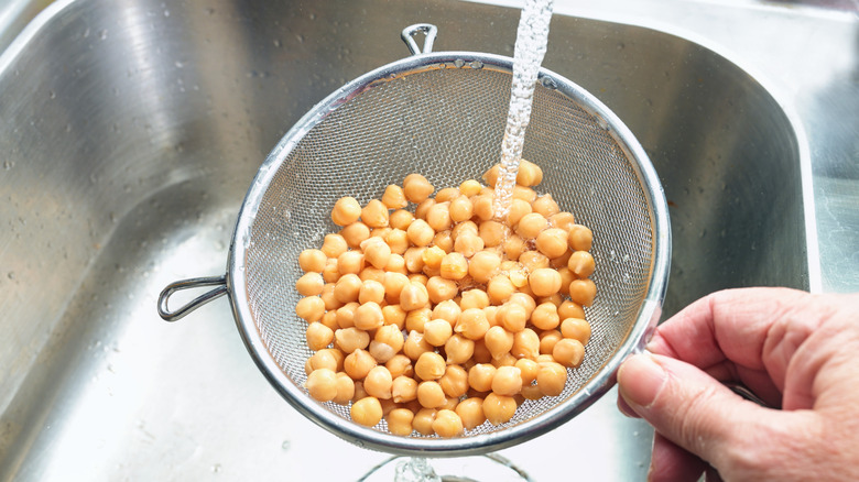 Canned chickpeas rinsing in a mesh strainer in the sink.