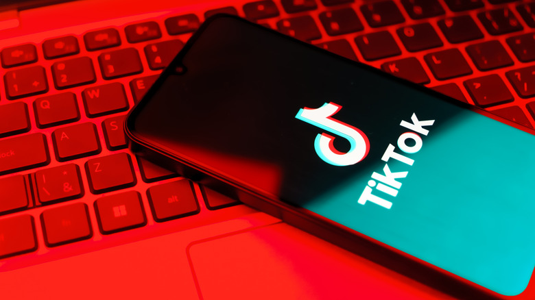 A phone showoing the TikTok logo on its screen, sitting on a keyboard with a red hue.