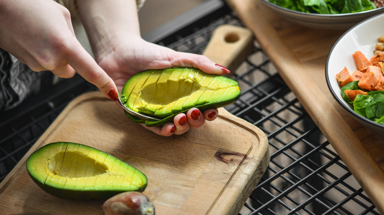 Somebody using a spoon to separate the flesh from the skin of an avocado