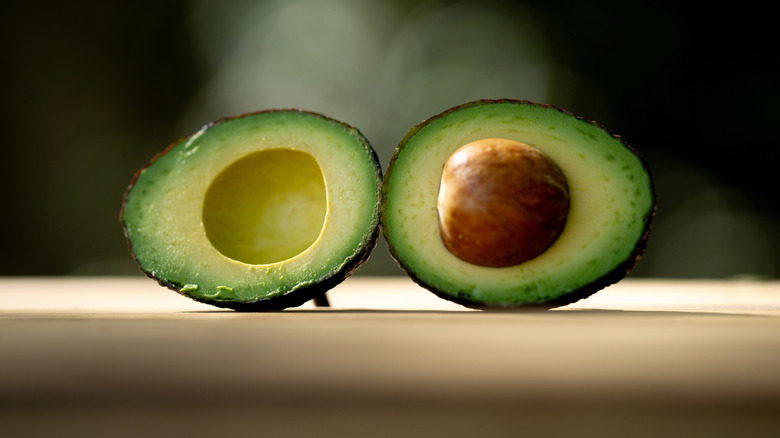 two halves of an avocado laid against a smoky black background
