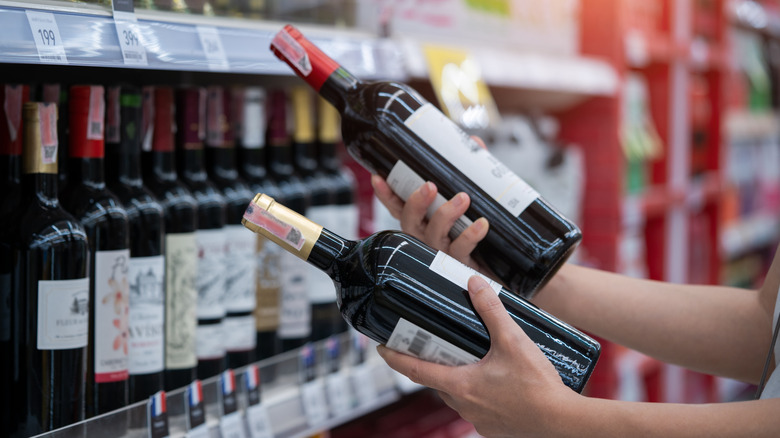 Shopper choosing between two bottles of wine, one red top, one gold top