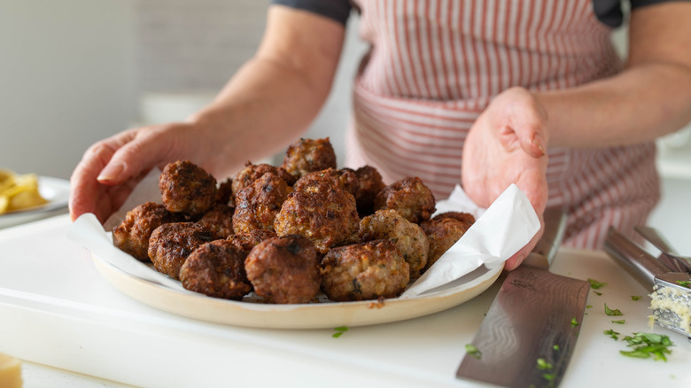 Cook with a plate of cooked meatballs.