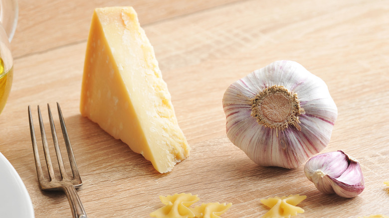 A piece of Parmesan cheese and a partial clove of garlic on a wooden cutting board.