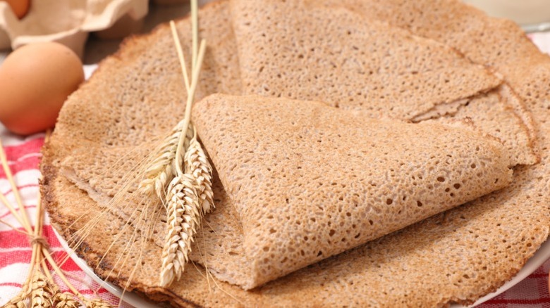 Thin buckwheat pancakes made the same thickness as crepes with some wheat and eggs surrounding them.