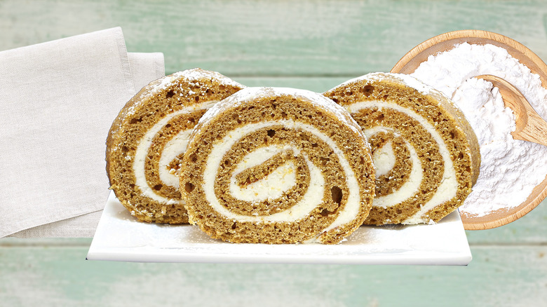 Slices of pumpkin roll in front of kitchen towels and a bowl of powdered sugar