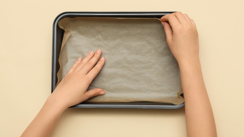 Hands preparing a pan with parchment paper