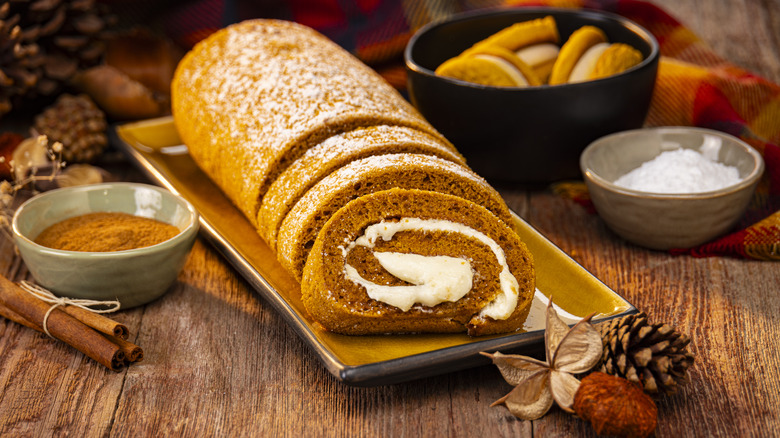 Pumpkin roll with three slices on a serving platter next to fall decor and spices
