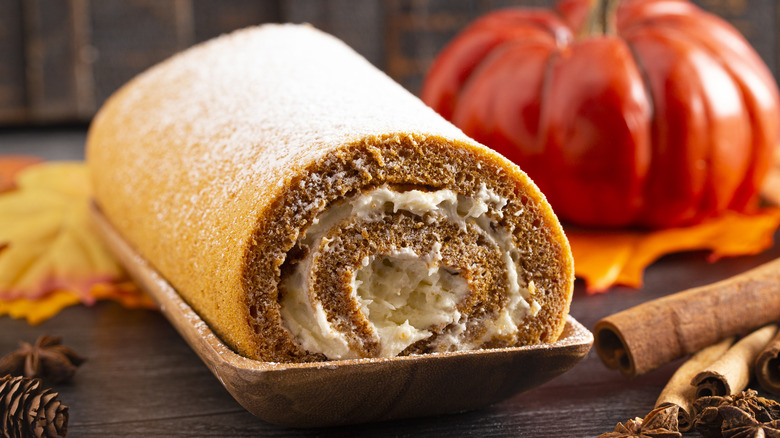A whole pumpkin roll on a wooden tray next to fall decorations