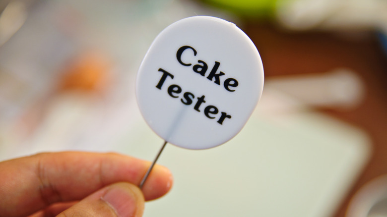 A hand holding a cake tester pick for baking