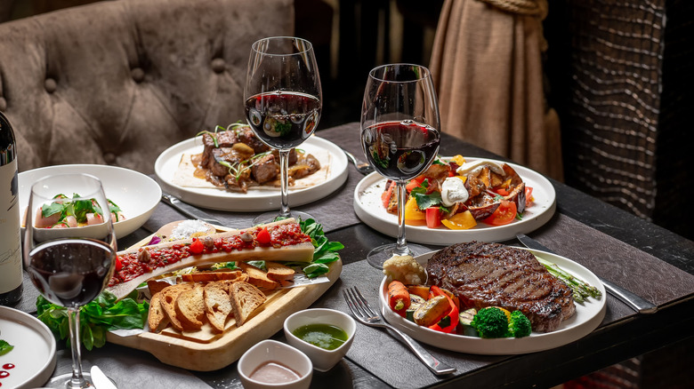 A table in a fancy restaurant filled with plates of food and glasses of wine