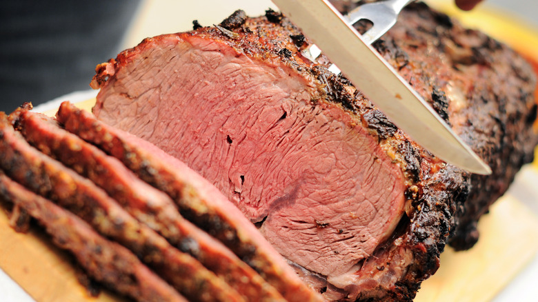 A close-up of a prime rib being sliced on a wooden cutting board