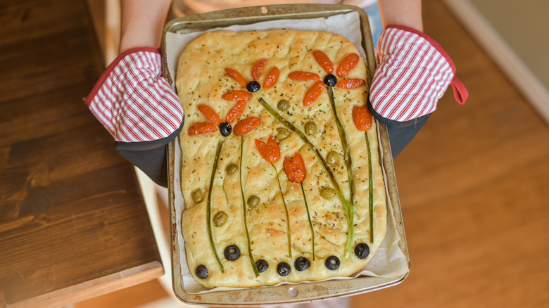Person holding a sheet pan of focaccia with toppings arranged like flowers