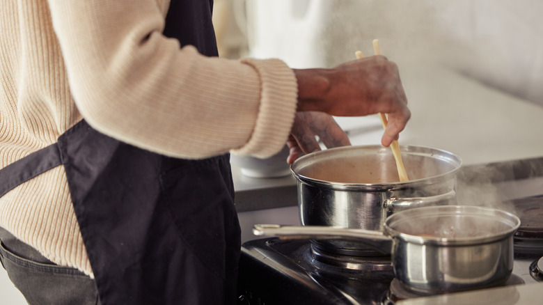 A person stirs the contents of a saucepan on the stove.