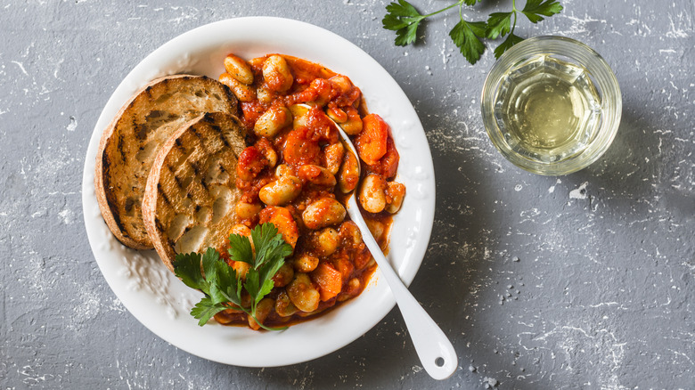 braised butter beans in tomato sauce with bread slices and a spoon