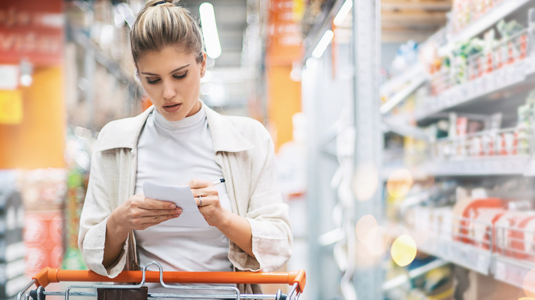 A woman reading from a shopping list at the grocery store.