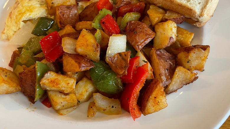 a plate of home fries with peppers and onions alongside an omelet and toast