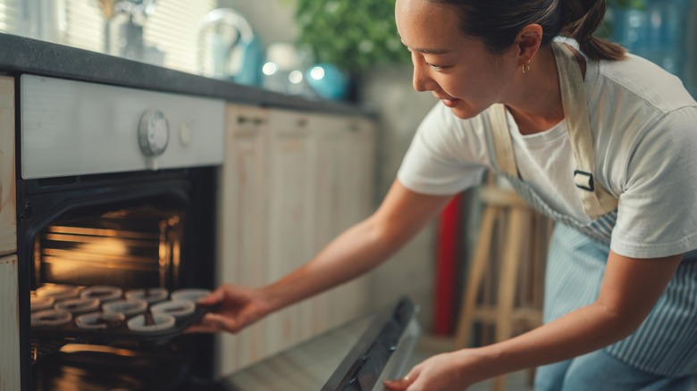 Woman putting a lined muffin pan into an oven