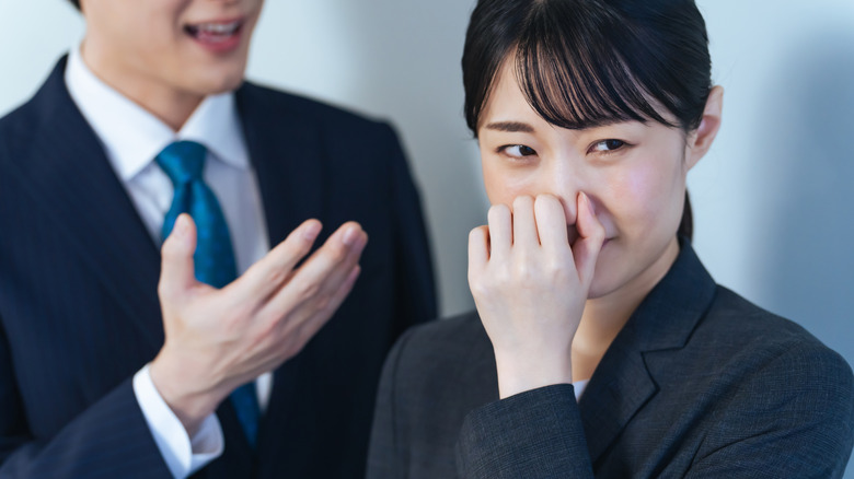 Businesswoman holding her nose and turning away from speaking colleague
