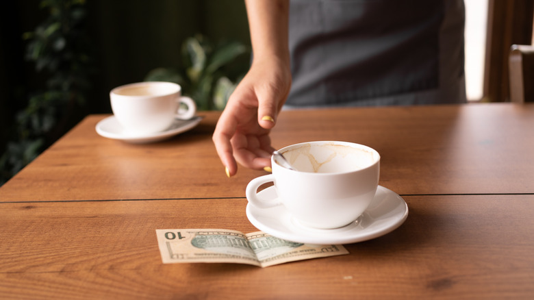 A server picking up a coffee cup with a tip left under it.