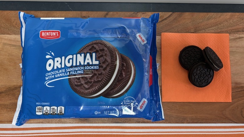 Benton's Original chocolate sandwich cookie package next to three cookies on an orange napkin