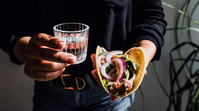 A person holding a taco and a glass of mezcal