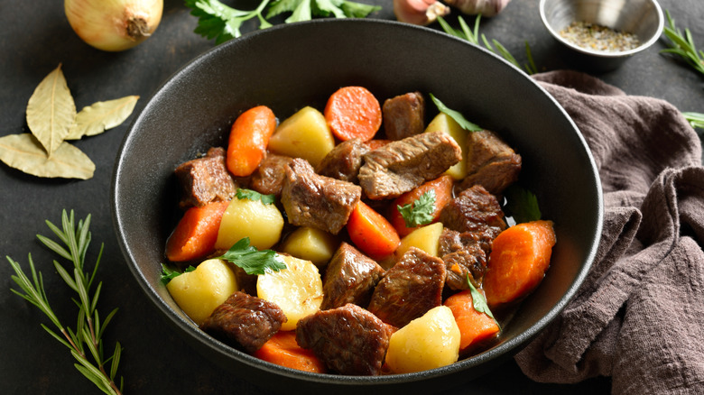A warm bowl of beef stew on a table with herbs and onions.