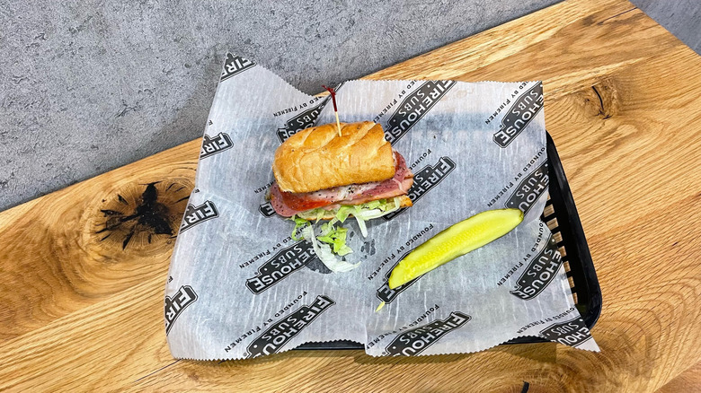 Italian sub and dill pickle spear in a black basket on wooden table