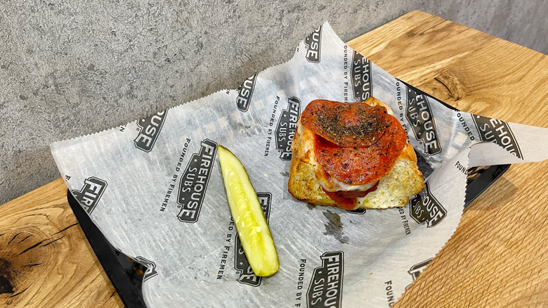 Pepperoni Pizza Meatball Sub and dill pickle spear in a black basket on wooden table