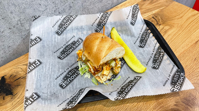 Spicy Cajun Chicken sub and dill pickle spear in a black basket on wooden table