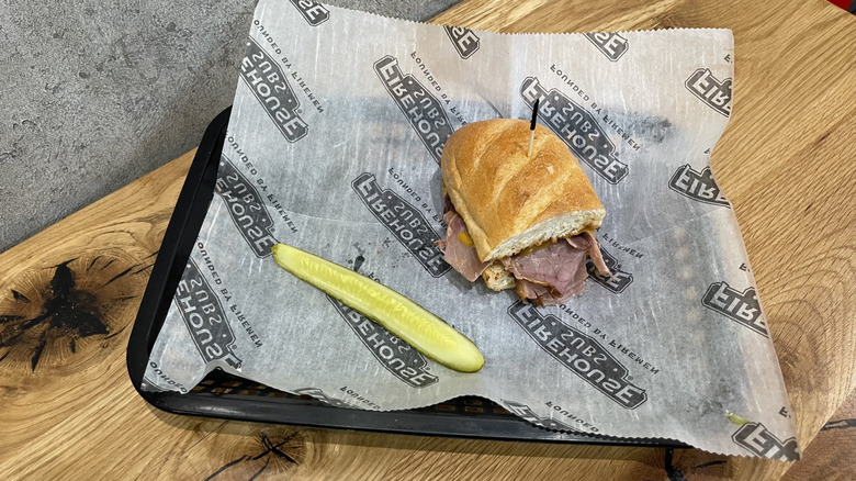 Smokehouse Beef & Cheddar Brisket sub and dill pickle spear in a black basket on wooden table