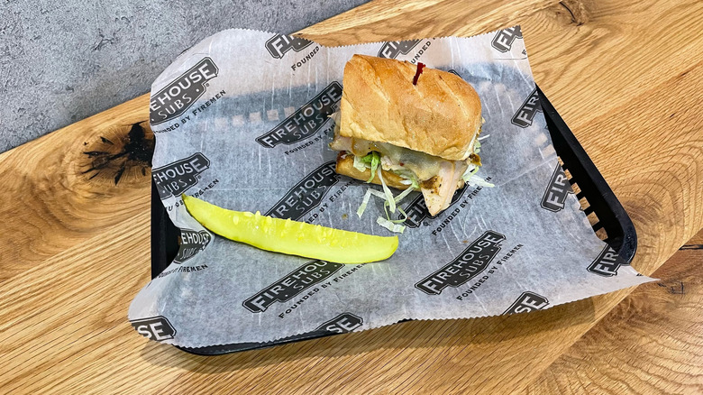 Jamaican Jerk Turkey sub and dill pickle spear in a black basket on wooden table