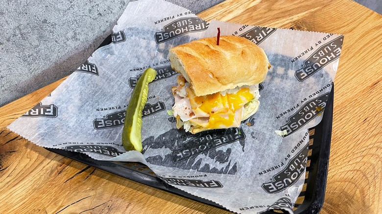 Turkey Bacon Ranch sub and dill pickle spear in a black basket on wooden table