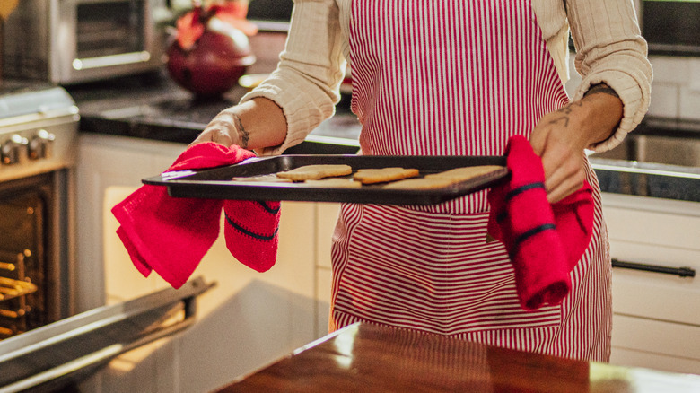 A person's hands are seen holding a sheet pan near an open oven door.