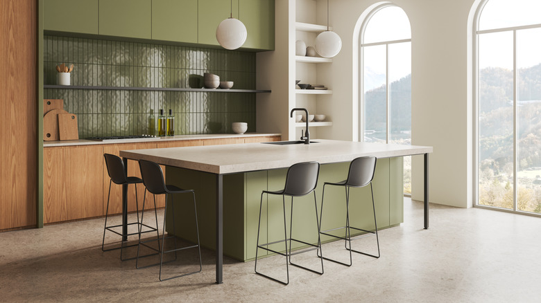 A clean and stylish kitchen with sage green and wood accents, enhanced with expansive windows for natural light