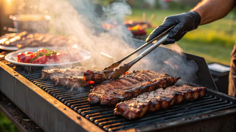 Pieces of juicy meat being cooked on the grill with visible smoke rising