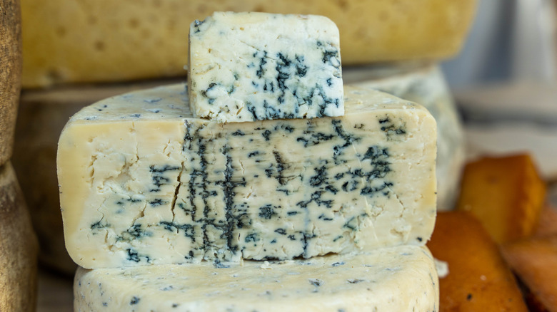 Round of blue cheese cut in half in front of other cheese in background.