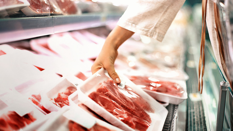 Hand selecting meat at grocery store