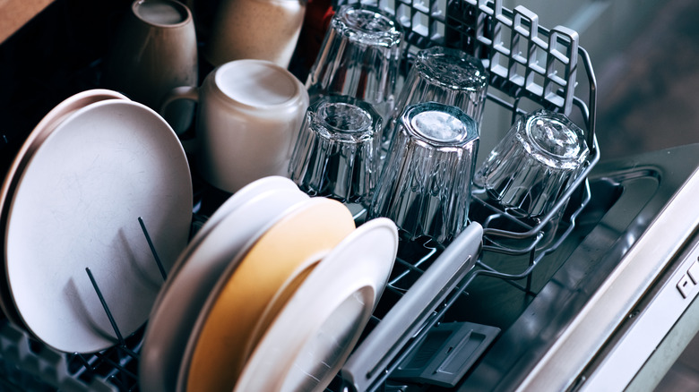 Open dishwasher filled with clean flatware and cups.