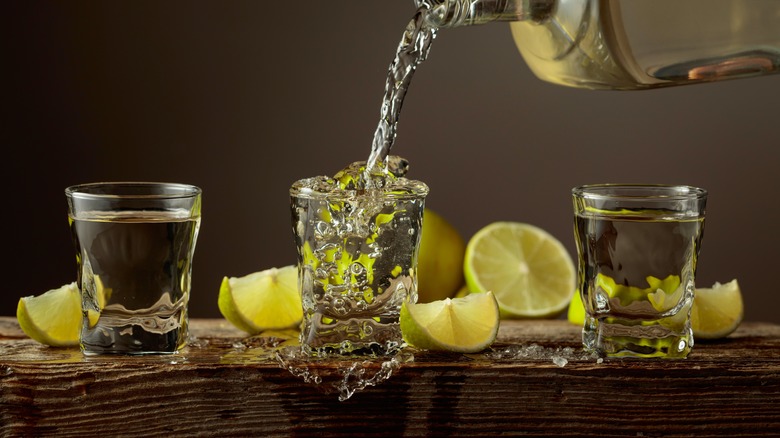Tequila poured into a shot glass with lime wedges
