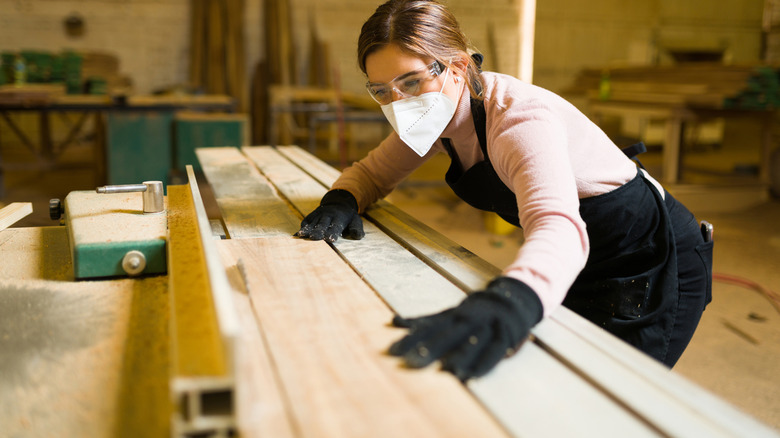 woman with gloves and mask cutting wood with table saw