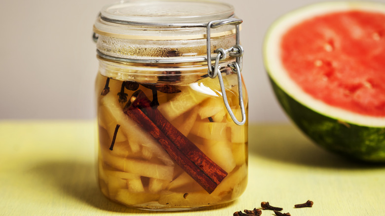 Pickled watermelon rind in jar with watermelon half in background