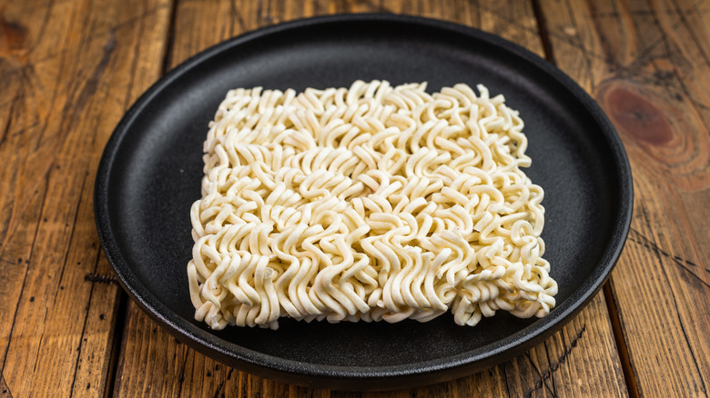 A block of instant ramen on a wooden table with a black plate.
