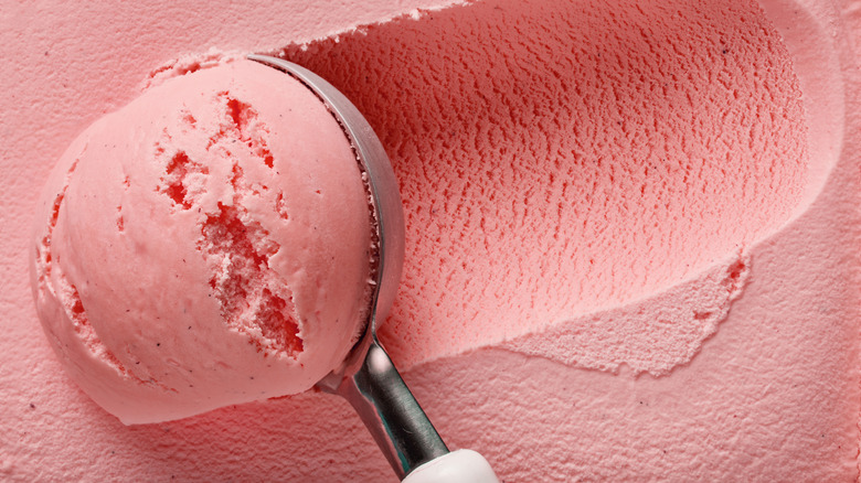 An ice cream scoop going through strawberry ice cream