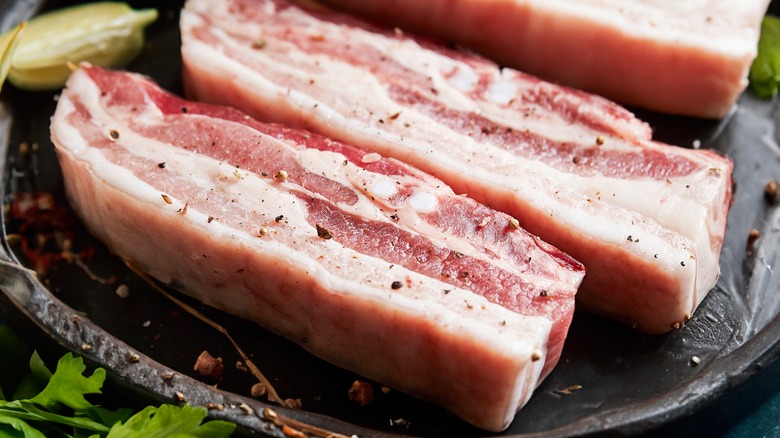 Slices of raw pork belly on a black stoneware plate.